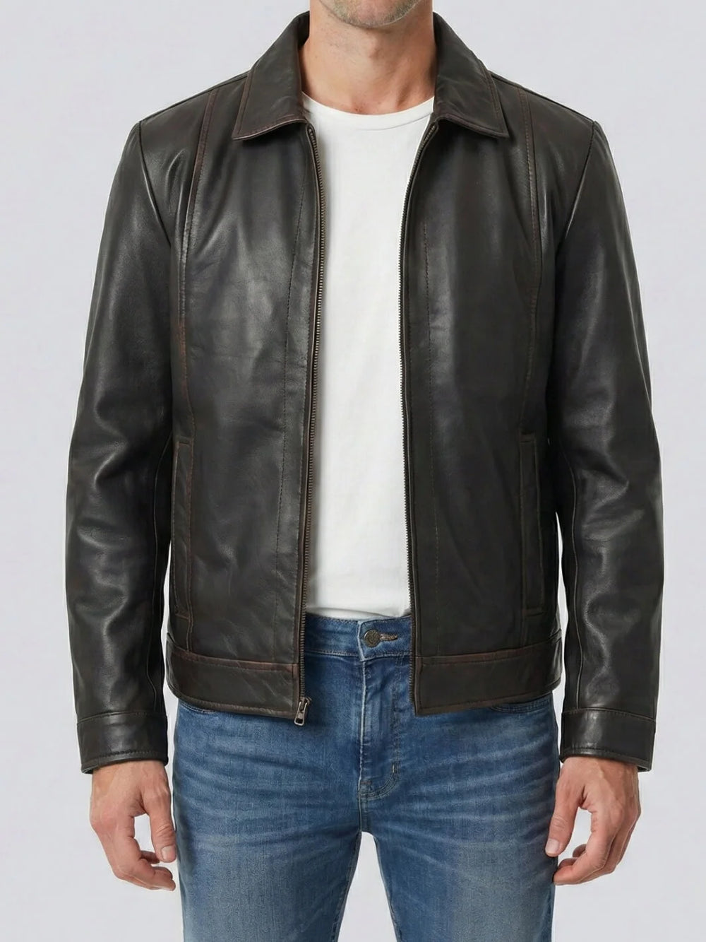 Man wearing a black leather jacket over a white shirt and blue jeans on a light gray background